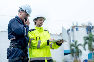 Birkaç petrokimya işçisi veya teknisyen, bir tanesiyle çalışmak için dizüstü bilgisayar kullanırken, aynı zamanda fabrikanın iş yerindeki iş arkadaşlarıyla iletişim kurmak için telsiz de kullanıyor..