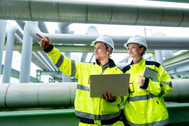 İki petrokimya veya gaz işçisi veya teknisyeninin yan görünüşü de insanoğlu ile birlikte boru ağının yanında çalışmak için dizüstü bilgisayar kullandıklarını gösteriyor..