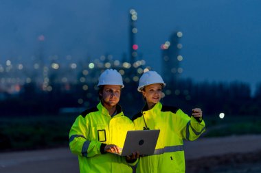 Gece çalışmak için dizüstü bilgisayar kullanan petrokimya işçileri ya da mühendisleri olan kadın ve erkek fabrikanın önünde ışıkla dikiliyorlar..