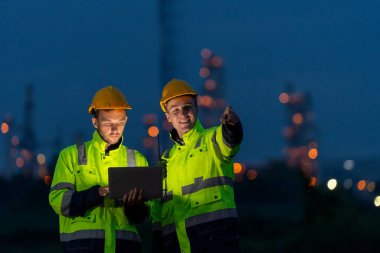 Petrokimya işçileri veya teknisyenler geceleri çalışmak ve fabrikanın önünde ışıkla durmak için dizüstü bilgisayar kullanıyorlar..