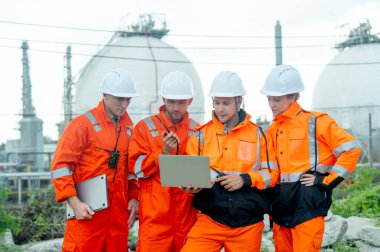 Bir grup gaz fabrikası teknisyeni ya da mühendis ellerinde bir dizüstü bilgisayarla işlerini tartıştılar ve gün ışığında tankın önünde durdular..