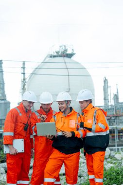 Gaz fabrikası teknisyenlerinin ya da mühendislerinin tek dizüstü bilgisayarlı dikey görüntüsü. İşlerini birlikte tartışacaklar ve gün ışığında tankın önünde duracaklar..