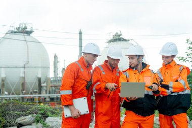 Gaz fabrikası çalışanları ya da mühendisleri bir dizüstü bilgisayarla işlerini tartıştılar ve gün ışığında tankın önünde durdular..