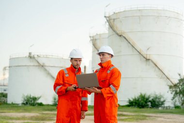 İki mühendis ya da gaz fabrikası teknisyeninin iş hakkında konuşmak ve iş yerindeki benzin deposunun önünde durmak için dizüstü bilgisayar kullanması.