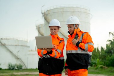İki teknisyen ya da gaz fabrikası işçisi gaz ya da petrokimya deposu önünde tartışıyor ve işlerinde mutlu görünüyorlar..