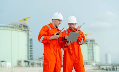 İki mühendis ya da gaz fabrikası teknisyenleri ellerinde telsiz ve dizüstü bilgisayarlarıyla işleriyle ilgili konuşmak ve gün ışığıyla körfezin yanındaki tankın önünde durmak için bekliyorlar..