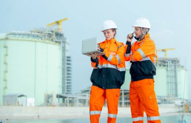 İki petrokimya veya gaz fabrikası işçisinin manzarası daha düşük. Koyun yanındaki fabrika deposunun önünde dizüstü bilgisayar kullanarak birlikte çalışıyorlar..