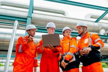 Bir grup petrokimyasal ya da gaz fabrikası işçisi ya da mühendisi dizüstü bilgisayarla çalışmayı tartışıyor ve fabrika işyerindeki boru hattının yanında duruyor..