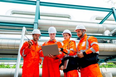 Düşük görüşlü petrokimya veya gaz fabrikası işçileri veya mühendisleri dizüstü bilgisayarla iş hakkında tartışıyor ve fabrika işyerindeki boru hattının yanında duruyorlar..