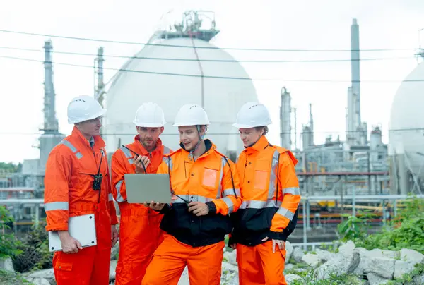 Bir dizüstü bilgisayarı olan bir grup gaz fabrikası teknisyeni ya da mühendisi birlikte çalışmalarını tartışır ve gün ışığında tankın önünde dururlar..