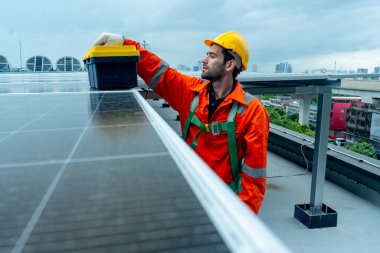 Mühendis ya da teknisyen, fabrika binasının çatısındaki kontrol ya da bakım sırasında güneş pili paneline alet çantası koymuş..