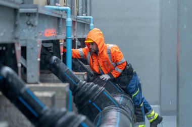 Fabrika işçisi ya da yağmurluk kontrollü teknisyen yağmur sırasında fabrika binasında bakım boru sistemi..