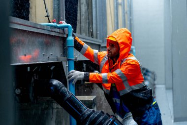 Yağmur yağdığı sırada fabrika binasında orta sınıf işçi ya da teknisyen yağmurluk denetimi ve bakım boru sistemi yapıyor..