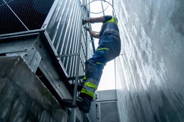 Fabrika işçisinin düşük görünümü fabrika binasının yanındaki çelik merdivenlere tırmanması sıcaklık kontrolüyle ilgili..