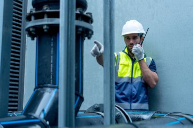 Mühendis ya da teknisyen iş arkadaşı ile iletişim kurmak için telsiz kullanıyor ayrıca fabrika inşaatının çelik boru sistemi üzerinde çalışırken de boruya işaret ediyor..