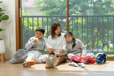 Asyalı anne, erkek ve kız çocukları ön tarafta cam kapının önünde oturuyor. Bir kızla anne ve oğlana yaslanıyor. Evlerinde pratik yaptıktan sonra bir elma yiyorlar..