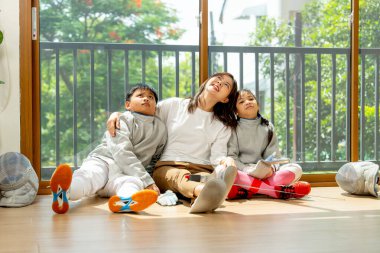 Asyalı anne, erkek ve kız aile olarak cam kapının önünde oturur ve evlerinde pratik yaptıktan sonra mutlulukla yukarı bakarlar..