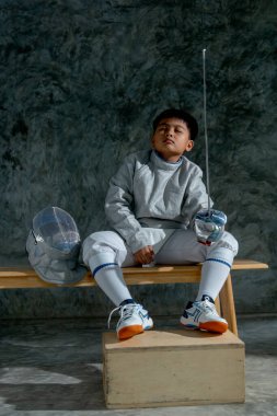 Eskrim üniformalı Asyalı çocuk idmandan sonra çişini tut ve tahta bankta otur..