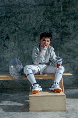 Eskrim üniformalı Asyalı çocuk ahşap bankta oturup yarışmayı kazanmak için mücadele ediyor..