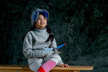 Eskrim üniformalı Asyalı kızı kapat. Çişini tut ve sol tarafına bak. Tahta bankta otur ve mutluluktan gülümse..