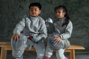 Eskrim üniformalı Asyalı erkek ve kız kardeşler ahşap bankta oturup ciddi duygularla kameraya bakıyorlar..