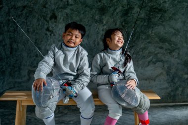 Eskrim üniformalı Asyalı kardeşlerimiz ahşap bankta oturur ve komik hareketler yaparlar. Yarışma antrenmanından sonra da dinlenirler..