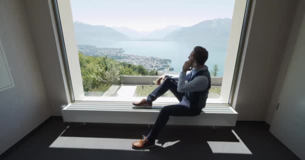 年轻的生意人在靠近窗户的现代化的办公室里用手机交谈 从那里可以看到湖山的全景 — 图库视频影像