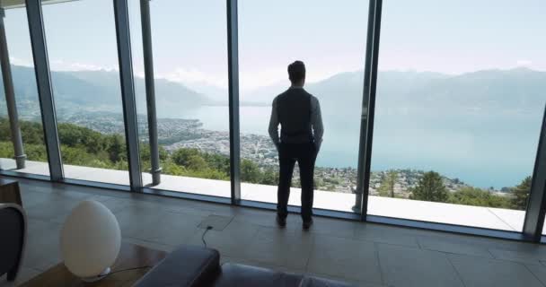Молодой Бизнесмен Современном Офисе Смотрит Окно Захватывающим Видом Озеро Горы — стоковое видео
