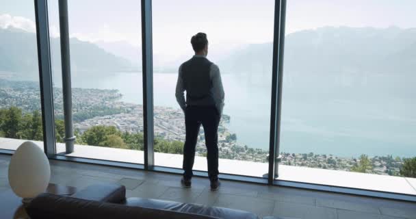 湖と山の息をのむような景色を窓から見る現代のオフィスで若いビジネスマン — ストック動画