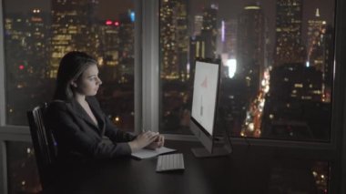 Modern Ofis 'te geceleri bilgisayar masasında çalışan kendine güvenen genç bir kadın. Yüksek kalite 4k görüntü