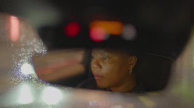 Gece vakti şehirde siyah kıvırcık saçlı, araba kullanan bir kadın trafik lambası. Yüksek kalite 4k görüntü