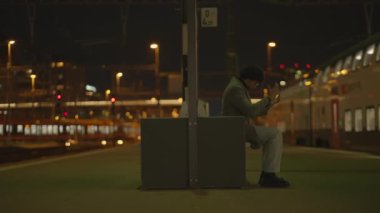 Siyah kıvırcık saçlı bir adam gece tren istasyonunda yalnız başına bekliyor. Yüksek kalite 4k görüntü