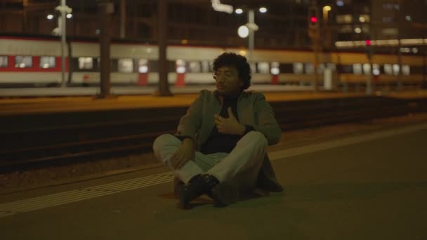 黒いカーリーの髪の男が夜に列車の駅で孤独待っています 高品質の4K映像 — ストック動画
