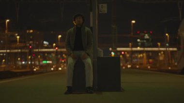 Siyah kıvırcık saçlı bir adam gece tren istasyonunda yalnız başına bekliyor. Yüksek kalite 4k görüntü