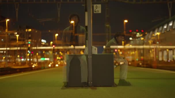 黒いカーリーの髪の男が夜に列車の駅で孤独待っています 高品質の4K映像 — ストック動画