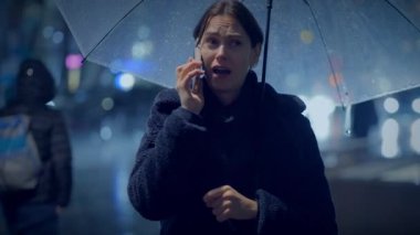 Yağmurlu bir gecede cep telefonuyla konuşan üzgün bir kadın.