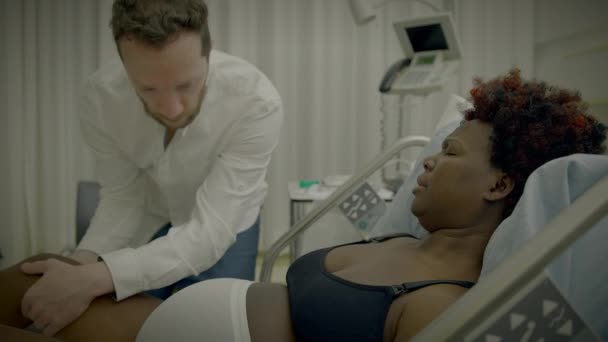 医師と話すクリニックベッドでカーリーヘアの横たわっている若いアフリカの女性 — ストック動画