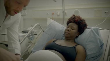 Klinikte yatan kıvırcık saçlı genç Afrikalı kadın doktorla konuşuyor.