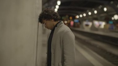 Siyah kıvırcık saçlı bir adam gece tren istasyonunda yalnız başına bekliyor. Yüksek kalite 4k görüntü