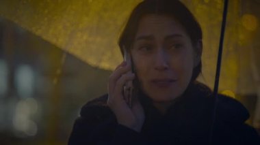 Yağmurlu bir gecede cep telefonuyla konuşan üzgün bir kadın.