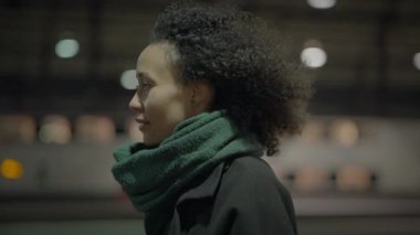Braun kıvırcık saçlı düşünceli bir kadın gece şehirde gezintiye çıkıyor.