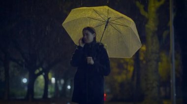 Yağmurlu bir gecede cep telefonuyla konuşan üzgün bir kadın.