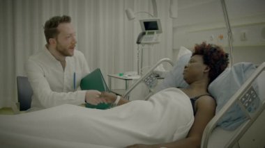 Klinikte yatan kıvırcık saçlı genç Afrikalı kadın doktorla konuşuyor.