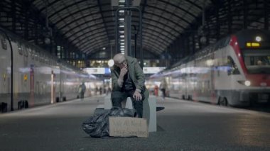 Yaşlılıktan muzdarip üzgün yaşlı erkek tren istasyonunda yalnız kalıyor.