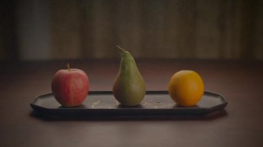 Armut da dahil olmak üzere üç meyve, ahşap bir masada bir tepside sergilenir. Bu doğal yiyecekler temel gıdadır ve temel besinleri sağlar.