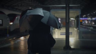 Bir adam ve bir kadın, bir tren istasyonunda elektrikli mavi bir şemsiye altında romantik bir öpüşme paylaşıyorlar. Yağmur seslerinin ortasında etrafları binalar ve arabalarla çevrili.