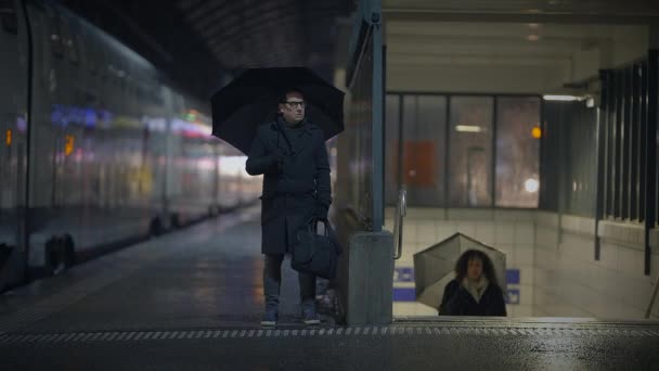 Mężczyzna Stoi Pod Szklanym Schronem Dworcu Kolejowym Trzymając Parasol Czekając — Wideo stockowe
