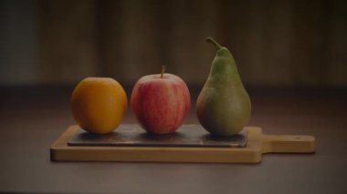 Bir armut da dahil olmak üzere üç meyve tahta bir kesme tahtasının üzerinde dinleniyor. Bu doğal yiyecekler birçok temel gıda yemeğinin temel bileşenleridir.