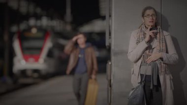 Anne, Oğlu Tren İstasyonu 'nda Bekliyor. Saate danışmak için saati kontrol ediyor.