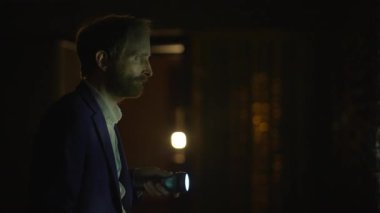 Takım elbiseli bir adam gece gözetleme yapıyor. Karanlık bir odada elinde fenerle banka kasasını inceliyor. Gergin atmosfer gizli ve riskli bir görevi işaret ediyor.